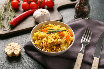 Bowl with tasty pilaf and ingredients on dark background