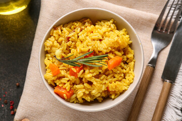 Bowl of tasty pilaf with rosemary and peppercorns on black background