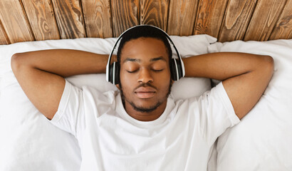 Relaxed African American Guy Listening To Relaxing Music For Sleep Wearing Wireless Earphones Lying...