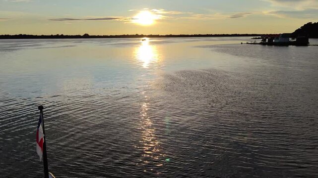Beautiful sunrise view from yacht cruising Amazon Jungle River with Amazonas state flag waving. Amazing sunset as seen from a boat side in the golden hours. Forest Silhouette. Amazonia, Brazil. 