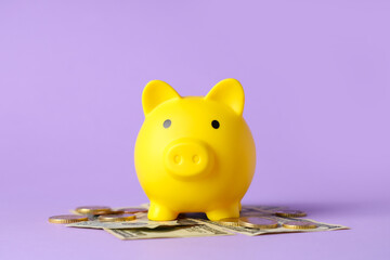 Yellow piggy bank with dollar banknotes and coins on lilac background