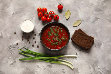 Bowl of tasty Ukrainian borscht with bread slices and ingredients on grey background