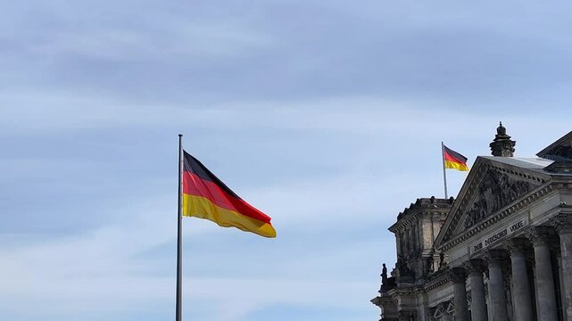 View of the German national flag waving proudly outside the historic Reichstag building in Berlin, Germany.	