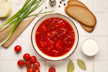 Bowl of tasty Ukrainian borscht and ingredients on white tile background