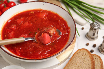 Bowl of tasty Ukrainian borscht and ingredients on white tile background, closeup