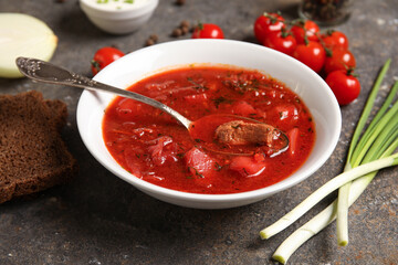 Bowl of tasty Ukrainian borscht with green onion and bread slices on dark background, closeup