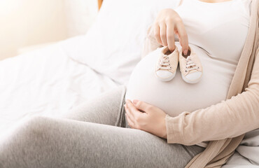 Pregnancy. Pregnant woman huggung her belly and holding small shoes near it, copy space
