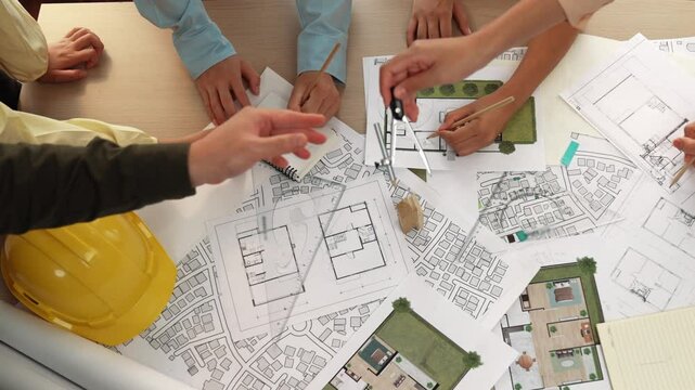 Architect and safety engineer discussion about building construction use blueprint on table with architectural document, measurement tool and wooden block scatter around at modern office. Delineation.