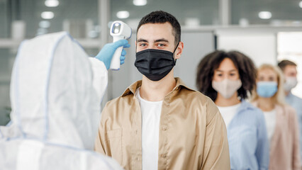 Checking temperature morning before work. Man in hazmat suit control first symptoms of illness at workers in protective masks in office, during covid-19 epidemic, empty space, close up