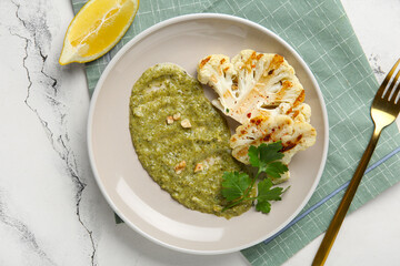 Plate of grilled cauliflower steaks with puree and parsley on white background