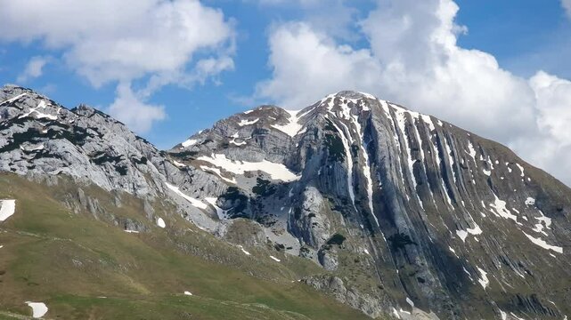 Mountain peaks in Prutas Durmitor Montenegro with snow patches time lapse. Reaching into blue sky and fluffy white clouds, capturing the beauty and tranquility of landscapes outdoors in spring season.
