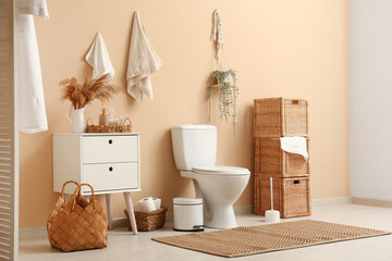 Interior of stylish restroom with ceramic toilet bowl, dresser and wicker baskets