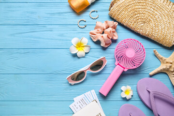 Female summer accessories and mini fan on blue wooden background with space for text