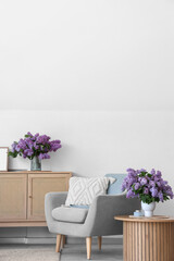 Interior of living room with armchair, table and lilac flowers in vases