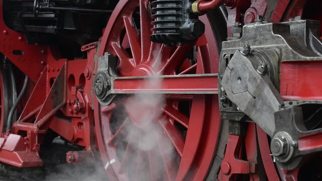 Close-up footage of antique steam train releasing steam clouds near its wheels.