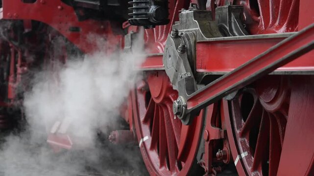 Close-up footage of antique steam train releasing steam clouds near its wheels.