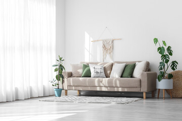 Obraz premium Interior of light living room with cushions on grey sofa and plants