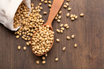 Soybeans scattered on rustic table with wooden spoon from paper bag, top view, free space