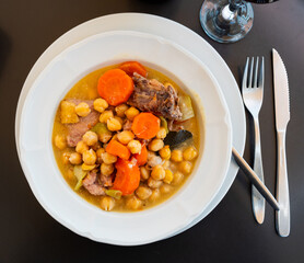 Plate with portion of hot chickpea and meat soup. First course is served with pieces of baguette..