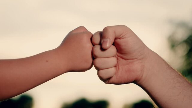 Two fists dad son trust friendship teamwork. Closeup. Father child clenching fists together. Dad kid friendly greeting with fist bump against sky. Parenting Parent child greeting each other with hands