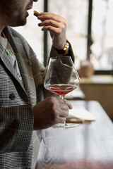 Champagne tasting in restaurant, A man holds in his hand a beautiful elegant glass with rose sparkling wine, He eats delicious snacks and drinks pink wine