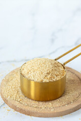 Nutritional yeast flakes in a measuring cup on white kitchen table. Close-up. Selective focus. Copy space. Vegan cheese substitute ingredient.