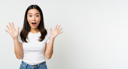 Surprised Asian Woman Raising Hands in Amazement on White Background