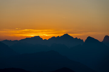 Sunset silhouettes of the mountains in the Dolomites Alps. Beautiful landscape of the rocky cliffs in Dolomiti Alps at sunset and sunrise light with some clouds red, orange and yellow color of sky