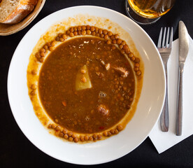 Spicy stewed lentils with suasage and vegetables with thick tomato sauce served in white plate. Typical Spanish cuisine