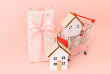Shopping cart with houses and gift box on a pink background.