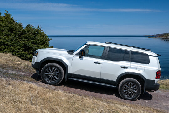 St. John's, Newfoundland, Canada-May 1, 2025: A white 2025 Toyota 1958 Land Cruiser off-road SUV hybrid vehicle parked on a rugged coastline with a view of the ocean. The premium vehicle is 4x4.