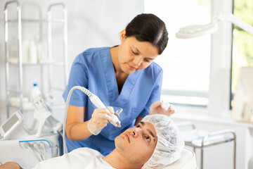 Fototapeta premium Young woman cosmetologist performs facial moisturizing procedure with apparatus young male patient