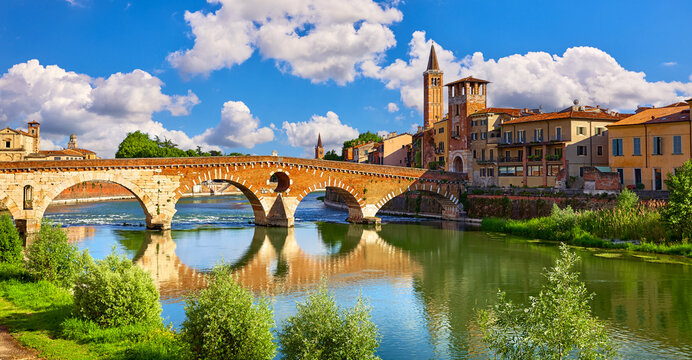 Verona, Veneto Region, Italy. Panoramic view at Bridge Ponte Pietra on Adige river. Sunny summer day panorama and blue sky with clouds. Ancient italian terracotta color houses.