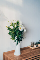 Fresh eustoma flowers bouquet in stylish white ceramic vase made in the shape of human hand on the wooden console. Trendy interior design decor details. Vertical card. Selective focus.