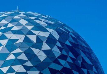 A blue and white spherical structure with triangular panels is viewed from a low angle against a clear blue sky.
