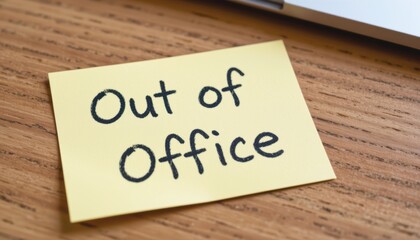 Sticky note saying "Out of Office" on wooden desk.