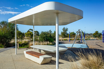 Contemporary outdoor picnic shelter with bench seating and nearby playground equipment in a...