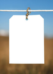 Blank invitation card on natural background. White empty frame, hanging tag with string on clothesline. Natural background.