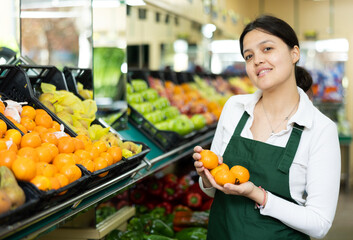Asian female seller in apron takes ripe large mandarin from window.Concept of proper nutrition,healthy lifestyle