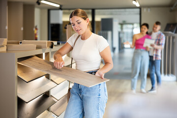Young woman buyer chooses sample of laminate flooring in hardware store