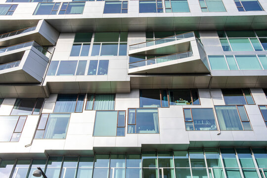 Asymmetric residential building facade with staggered balconies and white panels, representing innovative urban architecture and modular housing design for modern living. Photographed in Copenhagen.