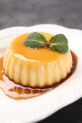 Delicious pudding with caramel sauce and mint on gray table, closeup