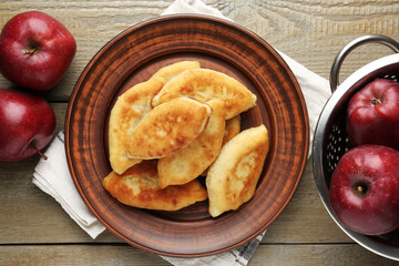 Delicious fried pyrizhky (stuffed pies) with apples on wooden table, flat lay