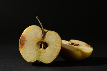 Halves of overripe apple on black background, closeup