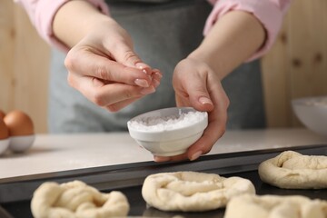 Woman putting salt onto raw pretzels at white table, closeup