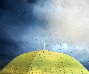 Yellow umbrella under cloudy sky, view through wet window. Stormy weather