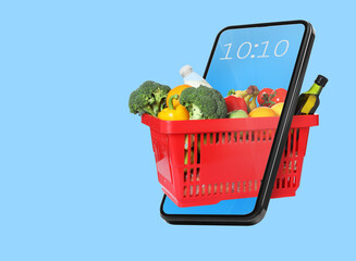 Red shopping basket full of food products coming through mobile phone screen on light blue...