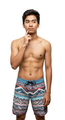 Fototapeta premium Young Asian man with a thoughtful expression, shirtless and wearing colorful patterned board shorts, posing against a transparent background in a studio setting.