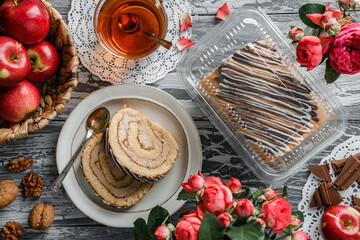 Delicious sponge roll cake stuffed with cream, nuts and apple on plate on light grey background with flowers. Sweets, dessert and pastry, top view