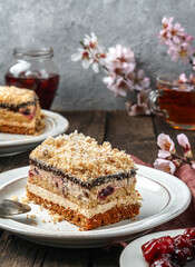 Piece of biscuit cake with cherry and cream on the plate over wooden background with jam and flowers. Sweets, dessert and pastry, homemade cakes, close up, selective focus
